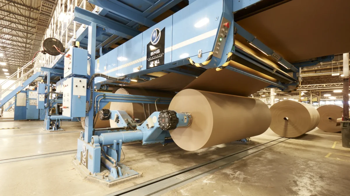 Industrial machinery processing large rolls of paper in a corrugated packaging facility